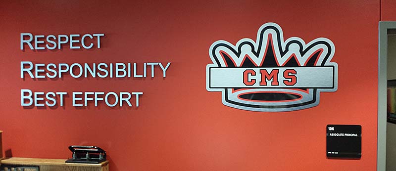 A bright red wall featuring the words "RESPECT," "RESPONSIBILITY," and "BEST EFFORT" in raised silver lettering next to a red, white, and black crown logo containing the letters "CMS."