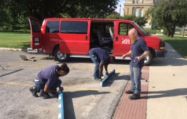 Three IPI workers installing curbs in a parking lot with a red IPI transport van in the background.