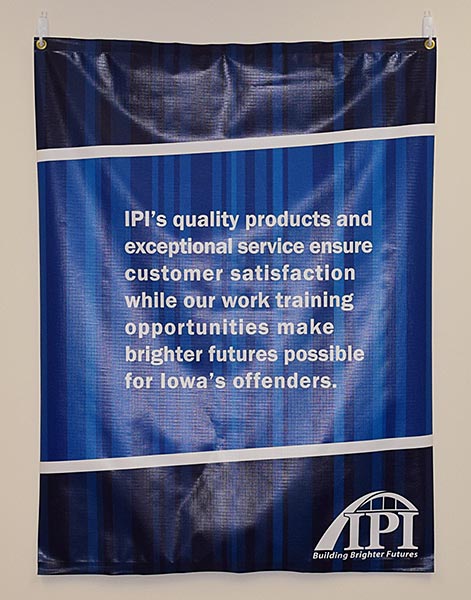 Hanging blue vinyl banner with grommets, IPI logo and text about IPI's quality products and mission.