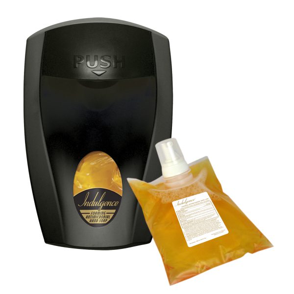 Black wall-mounted soap dispenser alongside a refill pouch of amber Indulgence foaming soap.