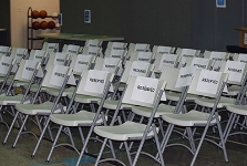 Rows of empty grey folding chairs set up for an event, each with a white paper sign reading "RESERVED" taped to the backrest.
