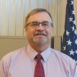 Headshot of IPI Director Bob Fairfax wearing a pink button up shirt and red necktie.