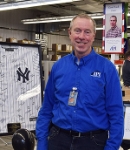 Dan Clark at the IPI Showroom next to a signed Yankees jersey in a display case with a banner that reads, "Good Luck, Dan" in the background.