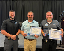 Luke Fowler standing next to Chad Bildstein and Keith Paulson in front of a black stage curtain holding their employee recognition certificates and acrylic awards.
